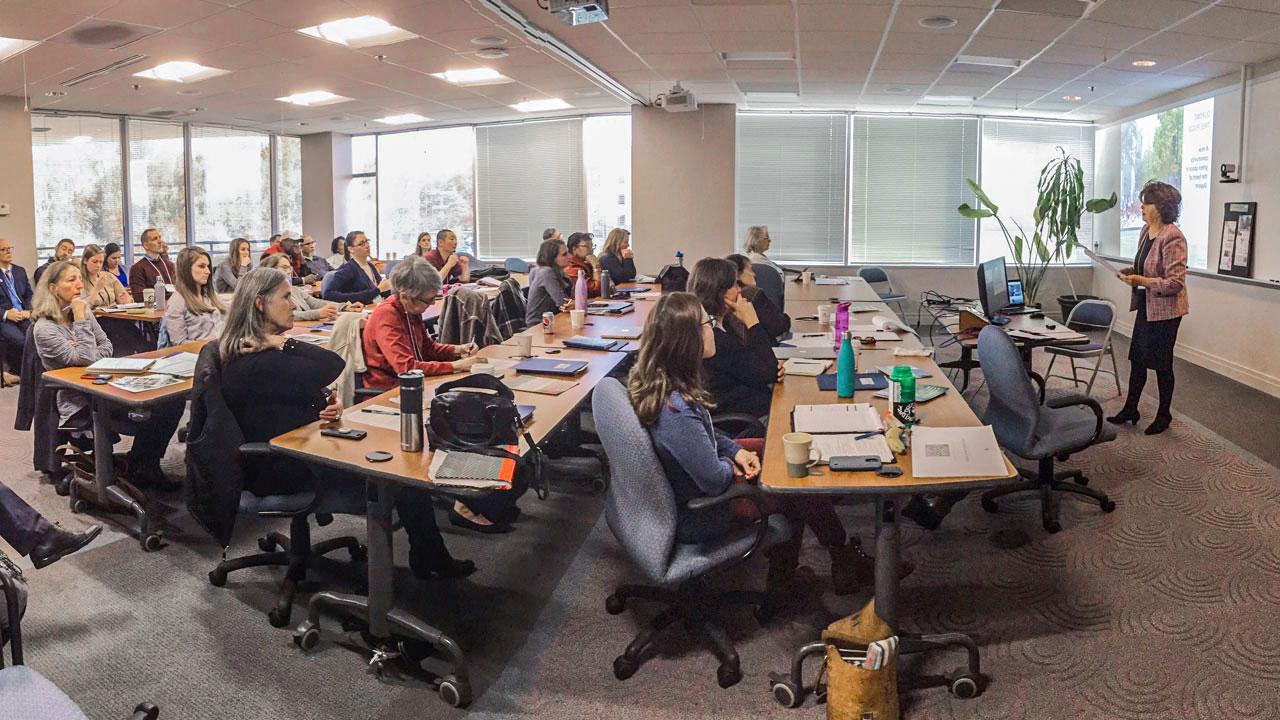 A side-view of a classroom filled with people listening attentively to a presenter